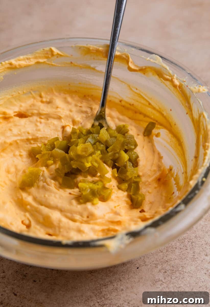 Spicy Deviled Eggs with Sriracha and Smoked Paprika 7 Deviled egg filling mixture in glass mixing bowl with chopped jalapeño over top.