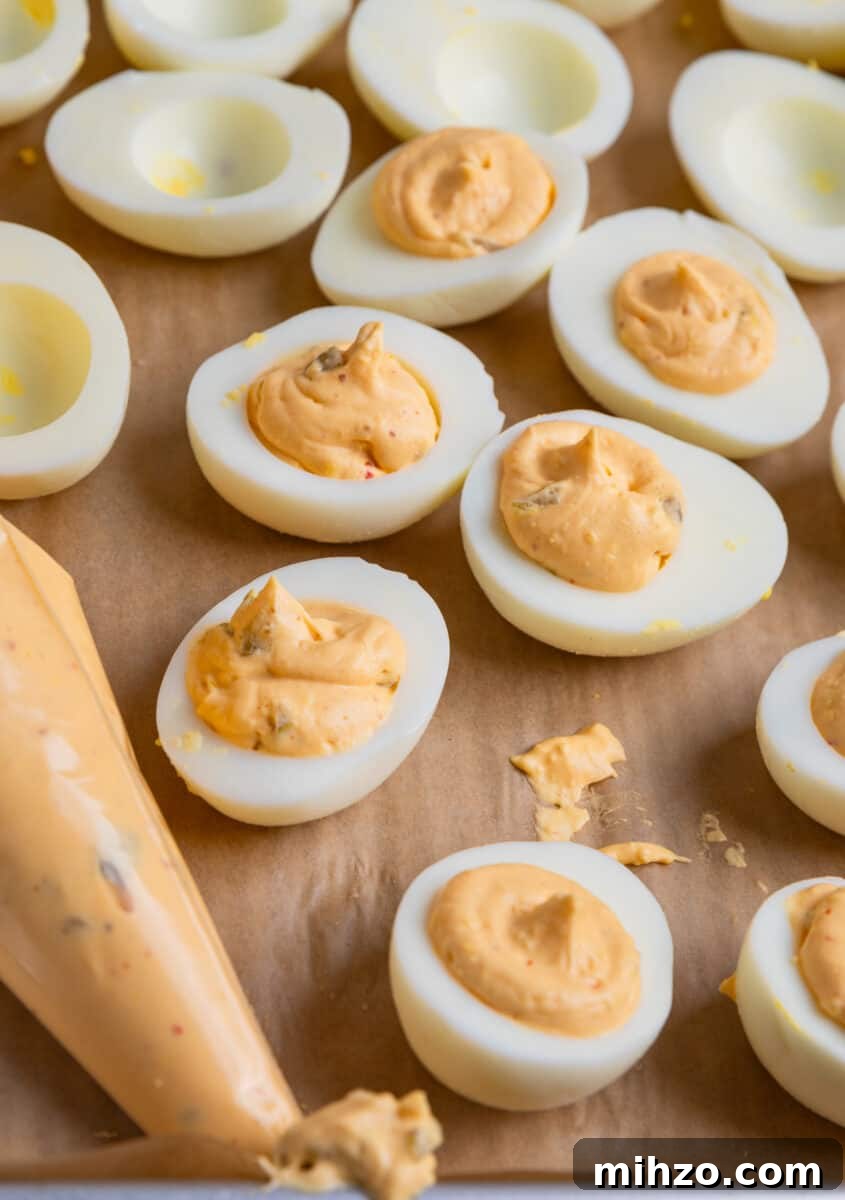 Spicy Deviled Eggs with Sriracha and Smoked Paprika 9 Boiled egg halves filled with egg yolk mixture with piping bag of yolk mixture beside them.
