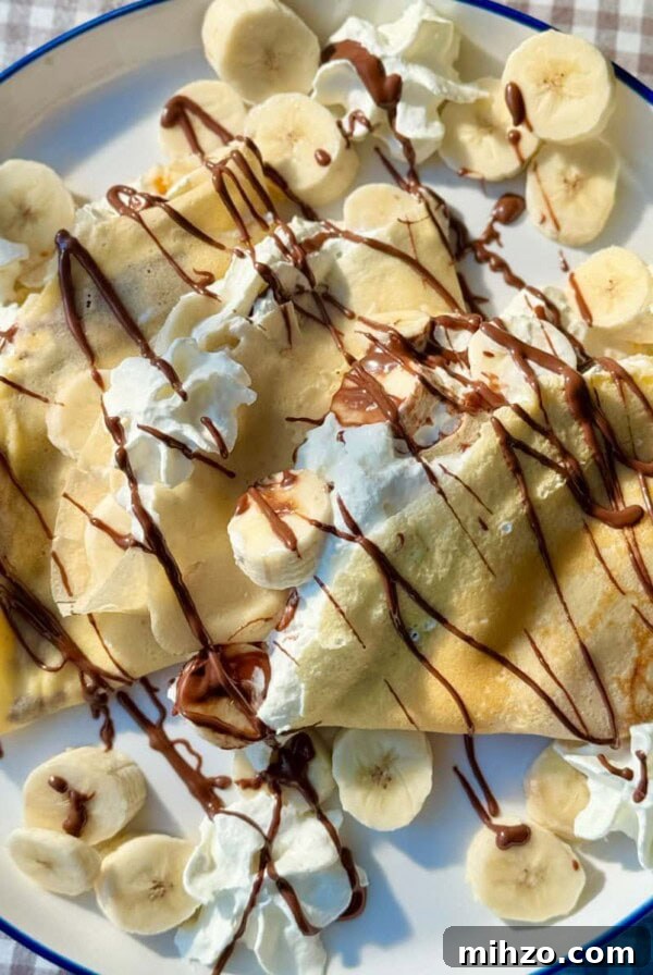 banana crepes on white plate with whipped cream and nutella.